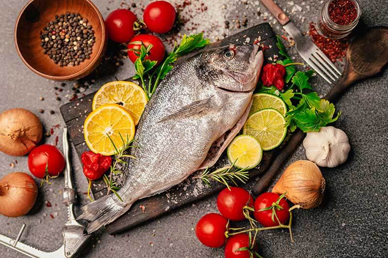 Fresh fish on a table being prepared with vegetables and seasoning